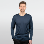 Eine Person mit kurzen Haaren lächelt in die Kamera. Sie trägt ein langärmeliges, dunkelblaues Hemd und eine schwarze Hose vor einem schlichten weißen Hintergrund.