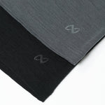 Zwei gefaltete T-Shirts in Grau und Schwarz liegen nebeneinander auf weißem Hintergrund. Jedes Shirt hat ein dezentes, geschwungenes Logo am Saum aufgedruckt.